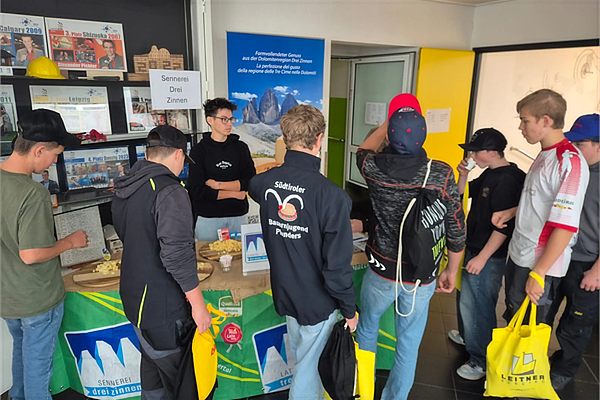 Unser Stand beim Wirtschaftstag am Berufsbildungszentrum Bruneck: Schülerinnen und Schüler am Tisch mit Käsewürfeln vor dem Rollup der Sennerei Drei Zinnen